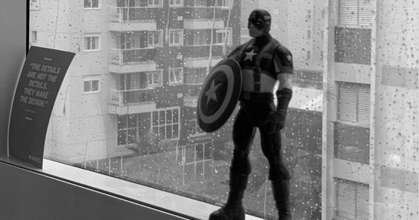 Janela molhada pela chuva, na beira um colecionável e do lado de fora vários prédios.